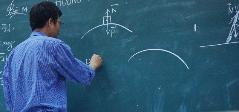 Profesor explicando un ejercicio de física en la pizarra.